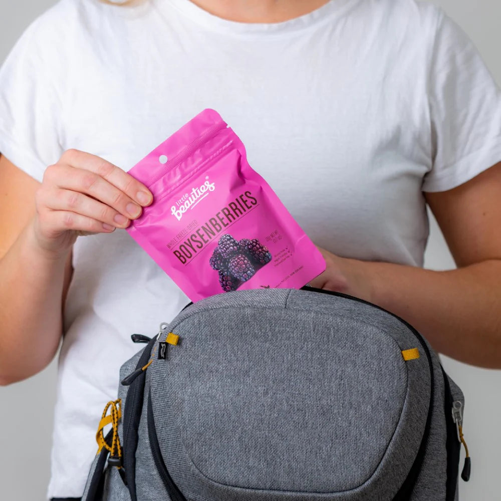 Person holding a pink package labeled Little Beauties 'Boysenberries' next to a gray bag on a plain background