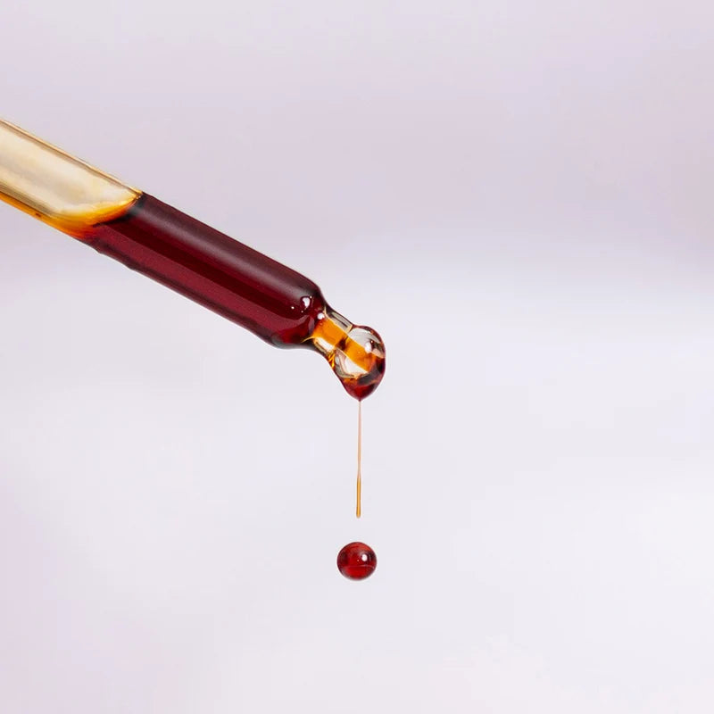 Close-up of a dropper with Manuka South propolis extract dripping on a light gray background