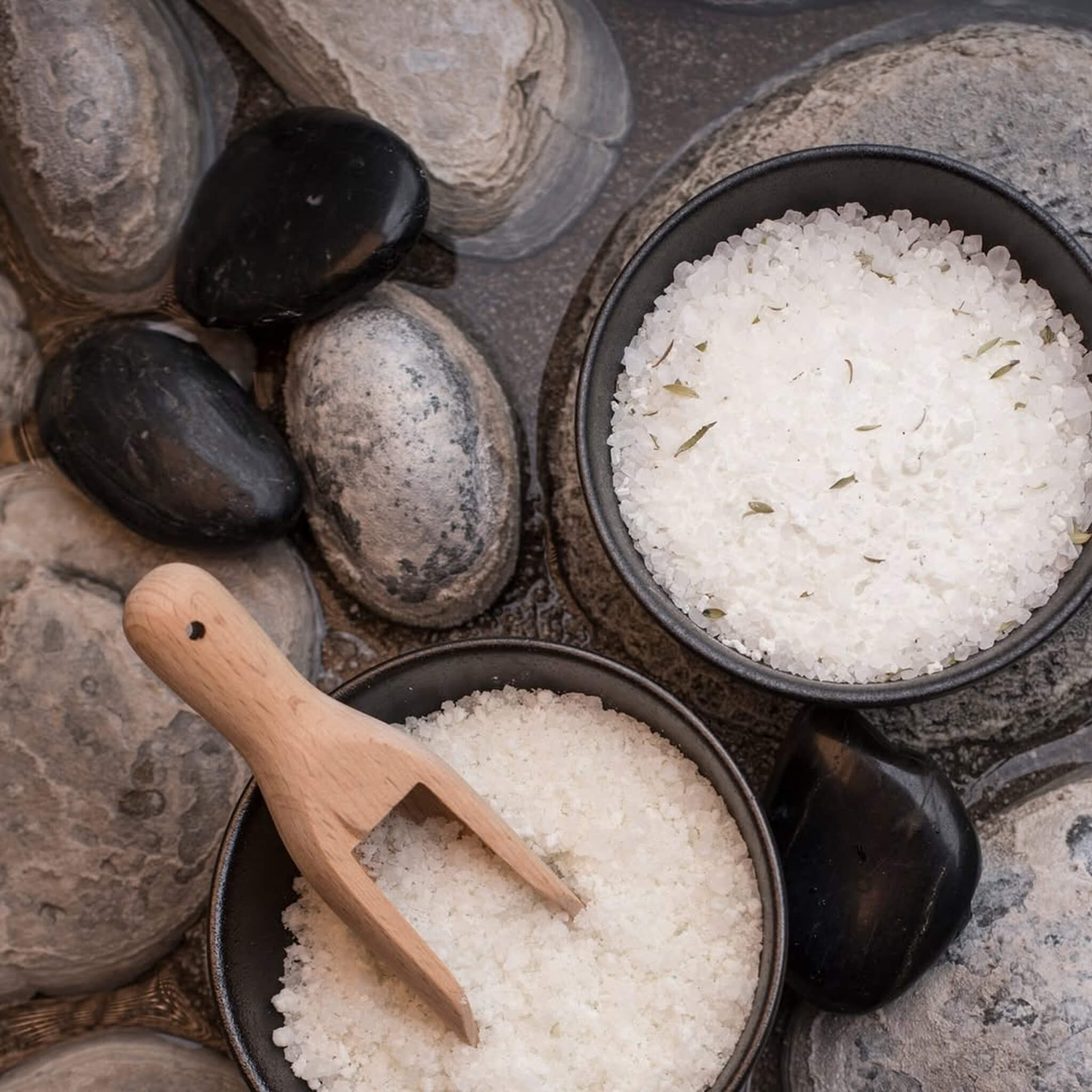Two bowls of Puresource thermal bath salt with a wooden spoon on a stone surface