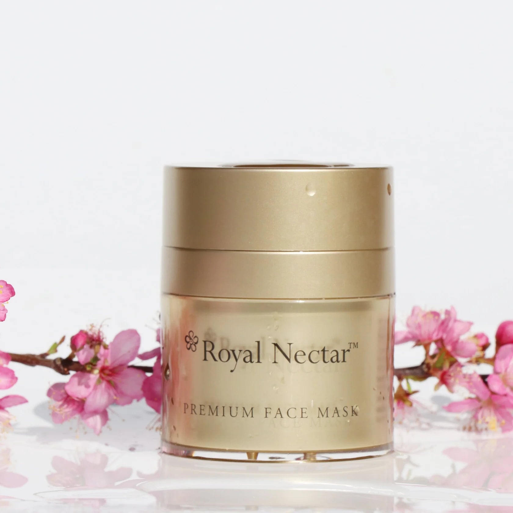 Gold jar of Royal Nectar premium face mask with pink flowers on a white background