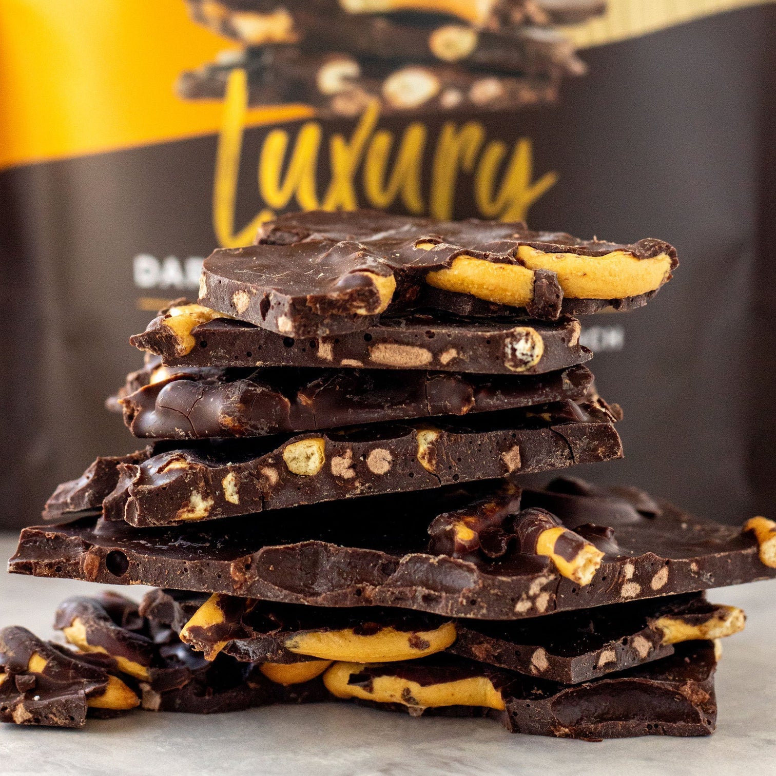 Stack of The remarkable chocolate dark chocolate bark pretzel and chocolate crunch against a package