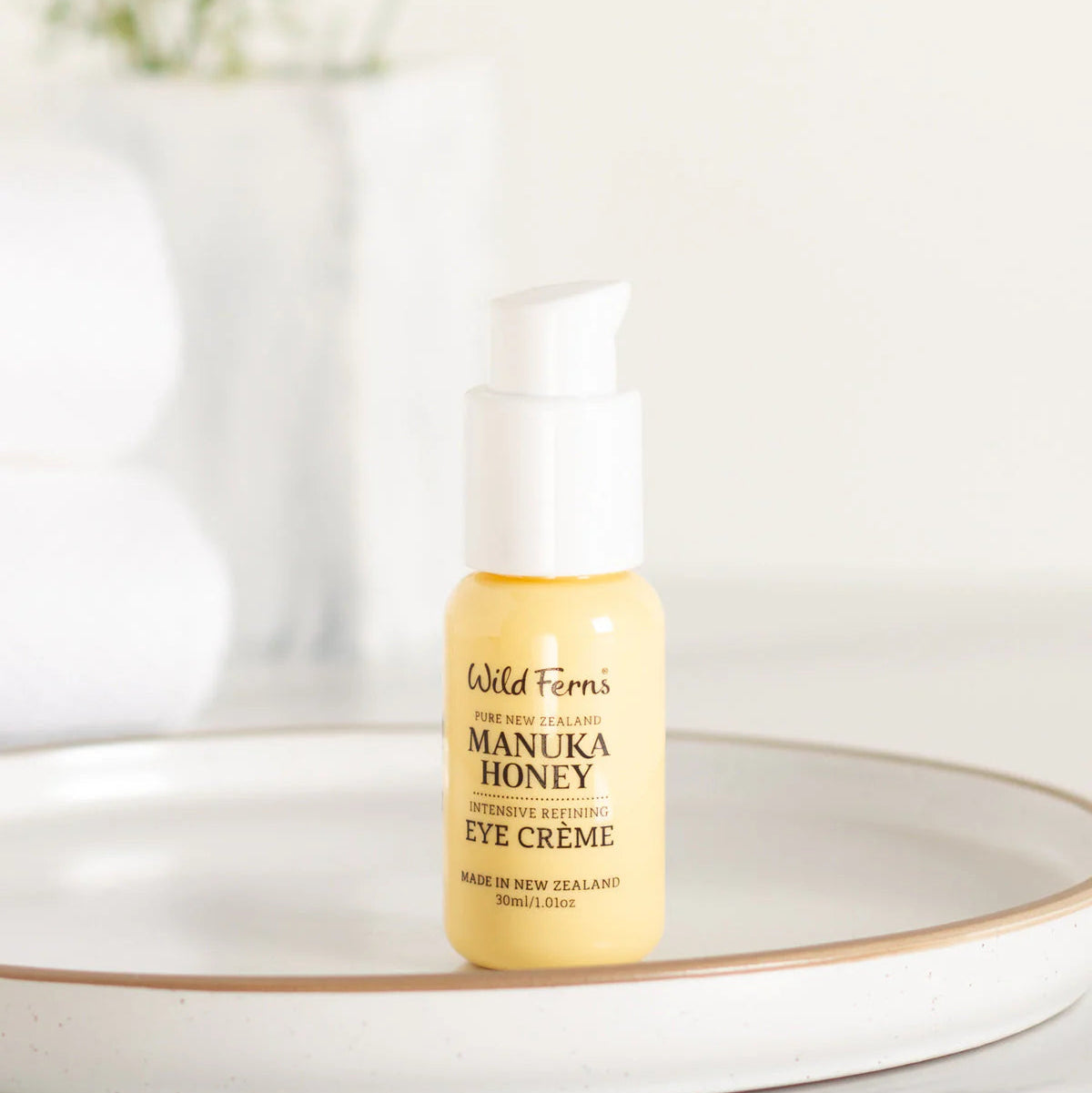 Wild Fern's Manuka Honey Eye Crème bottle on a white surface with a blurred background