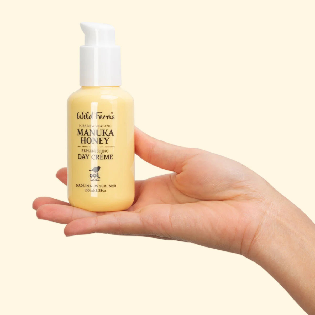 Hand holding a bottle of Wild Ferns Manuka Honey Day Creme against a beige background