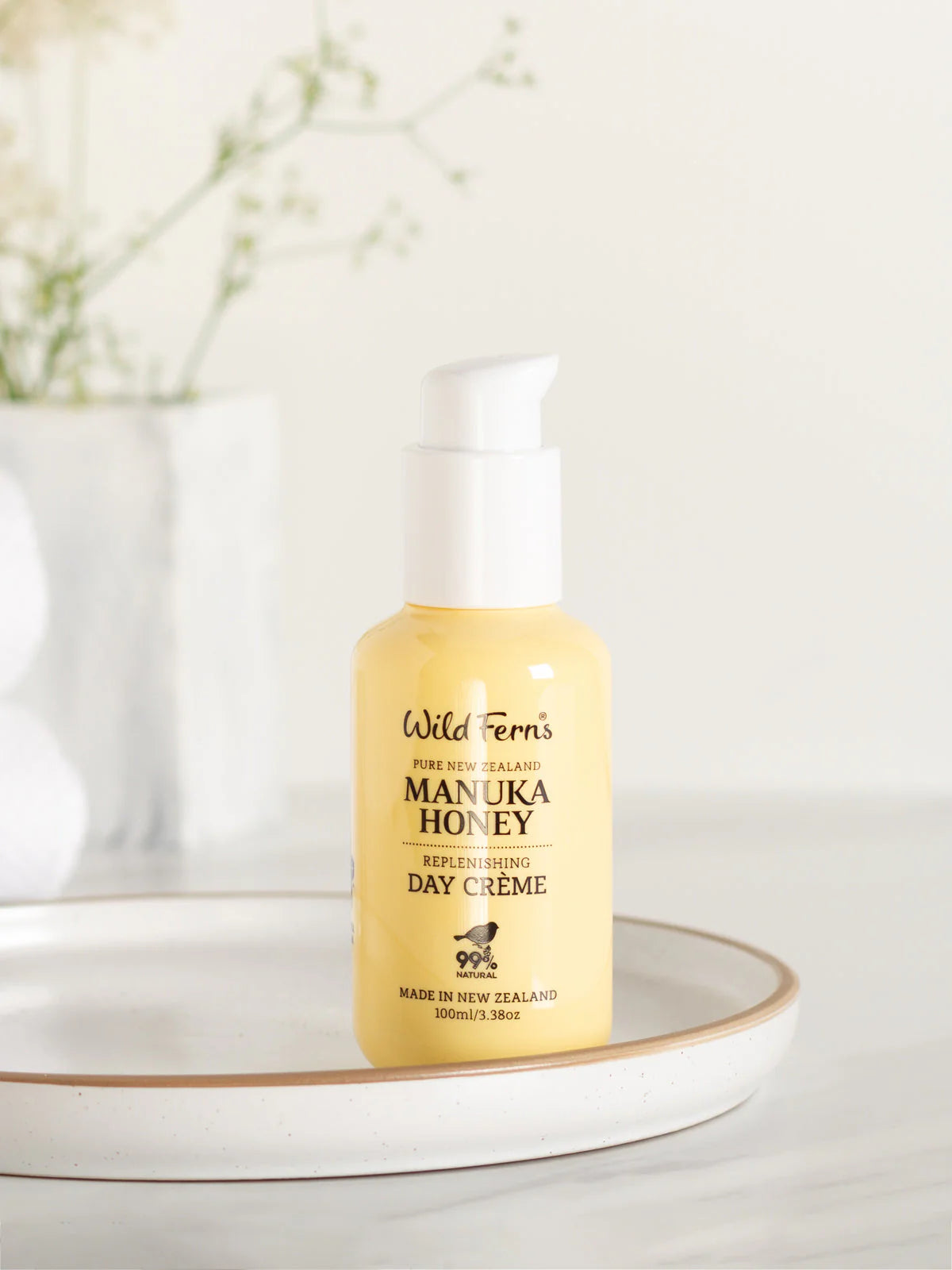 Yellow bottle of Wild Fern's Manuka Honey Day Creme on a white surface with a blurred background