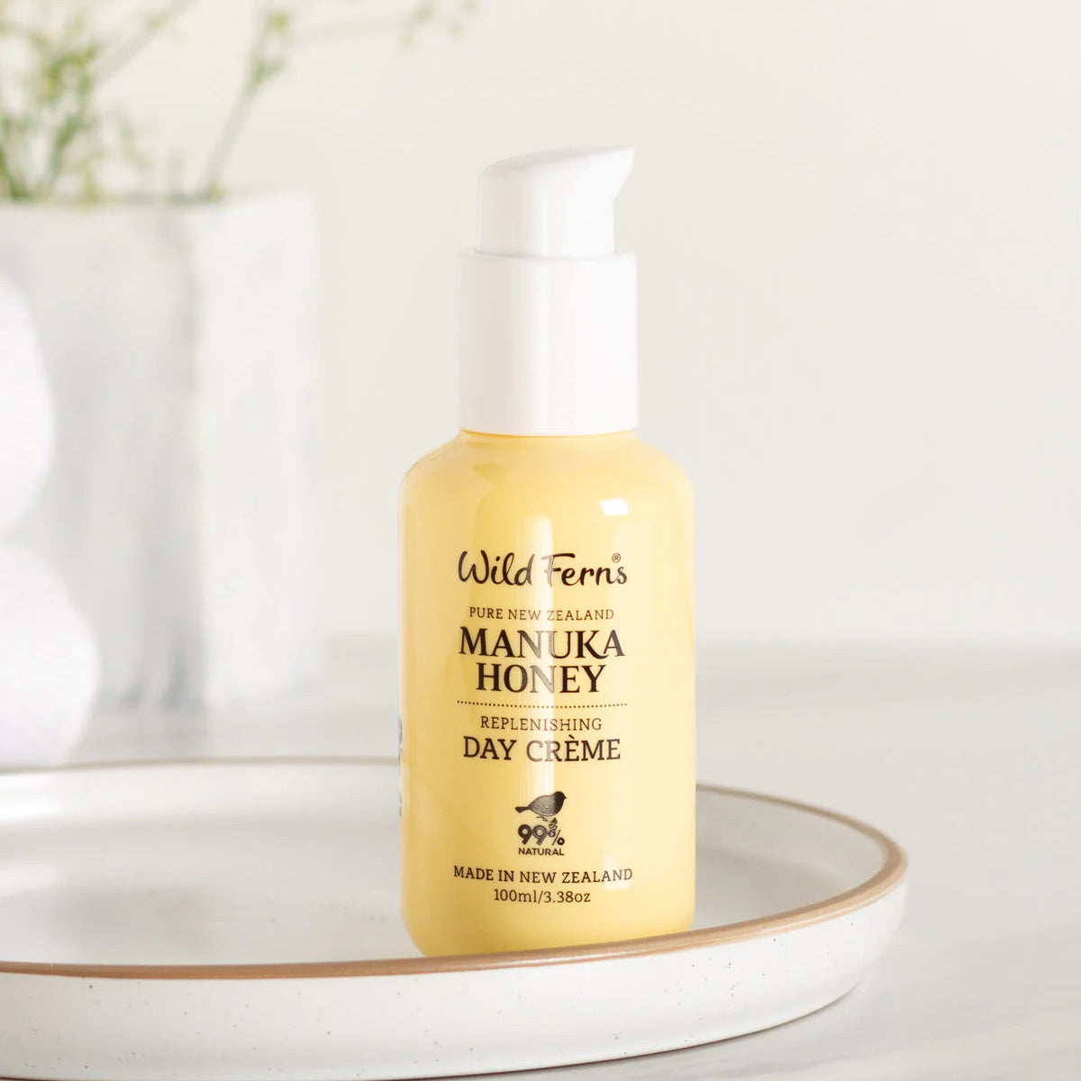 Yellow bottle of Wild Ferns Manuka Honey Day Creme on a white surface with a blurred background