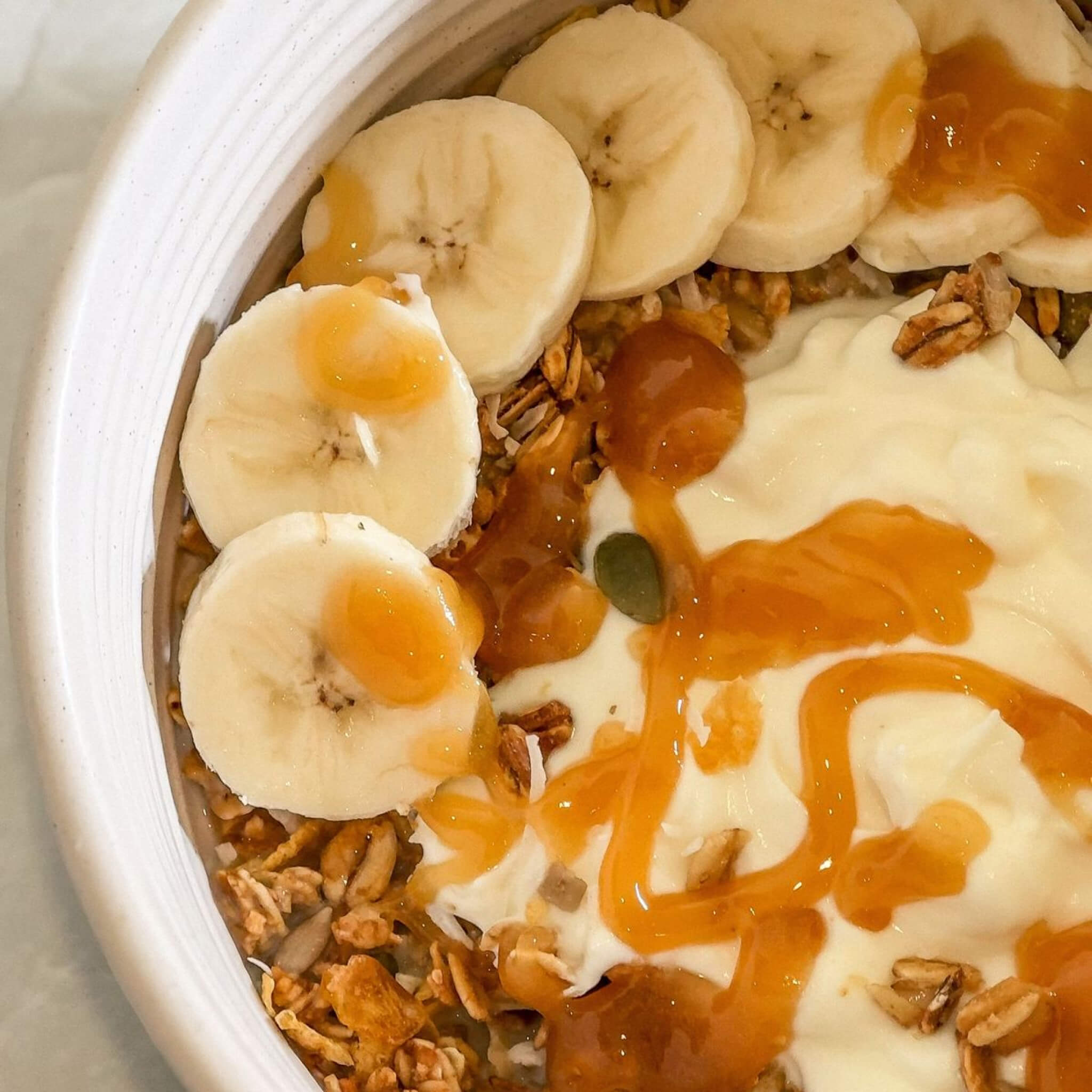 Yogurt bowl with granola, bananas, and Steens Manuka Honey on a white plate.