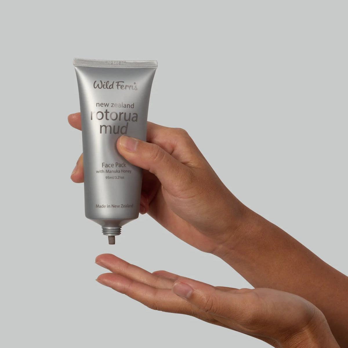 Hand holding a tube of Wild Ferns Rotorua mud product against a gray background