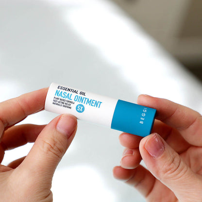 Hand holding a small container of nasal ointment with a blue and white design.