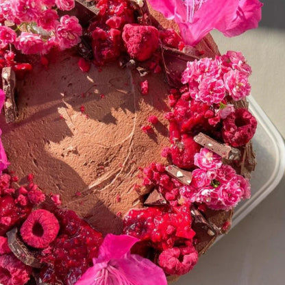 Chocolate cake decorated with pink and red flowers and little beauties freeze dried fruits on a white plate.