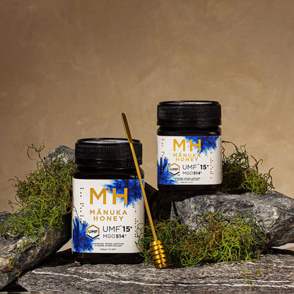 Two jars of M&H Manuka Honey UMF 15+ 250g and 500g with a honey dipper on a natural stone background.