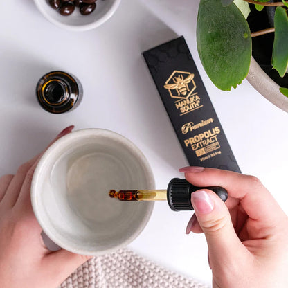 Person using a dropper to add Manuka South propolis extract from a branded bottle into a white cup.