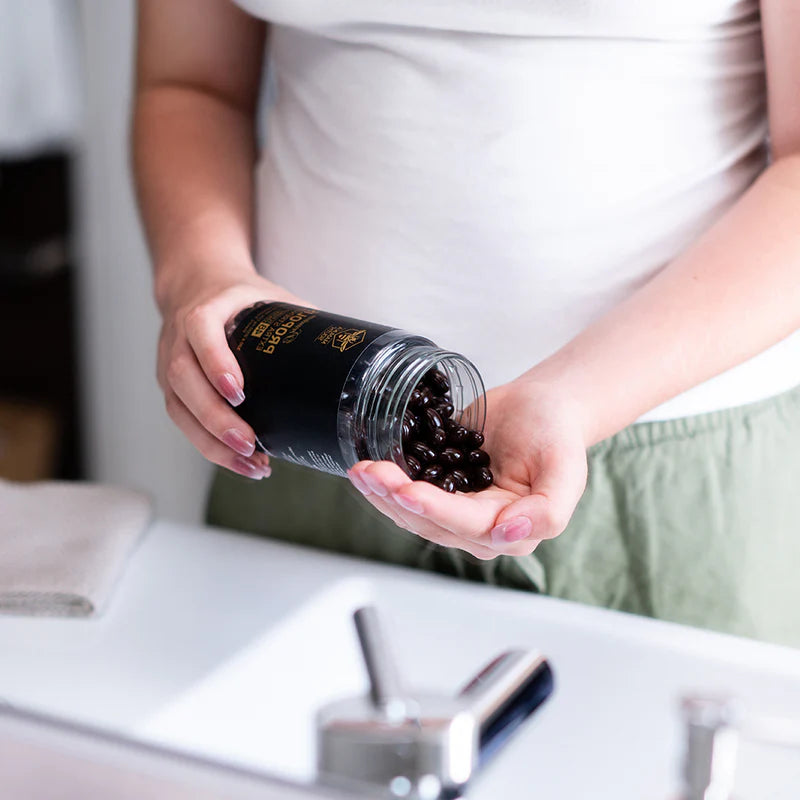 Person holding a container of Manuka South Propolis Soft Gel Extra Strength over a kitchen counter.
