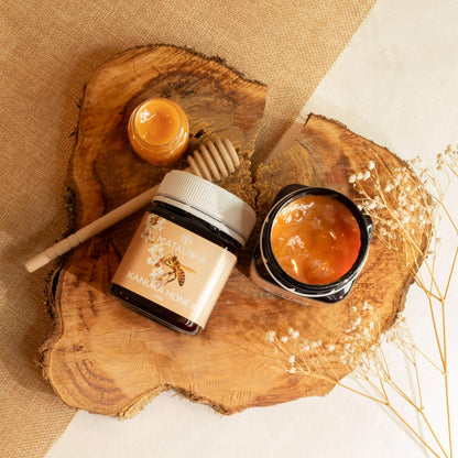 Three jars of honey on a wooden surface with a Matauwhi kanuka honey dipper.
