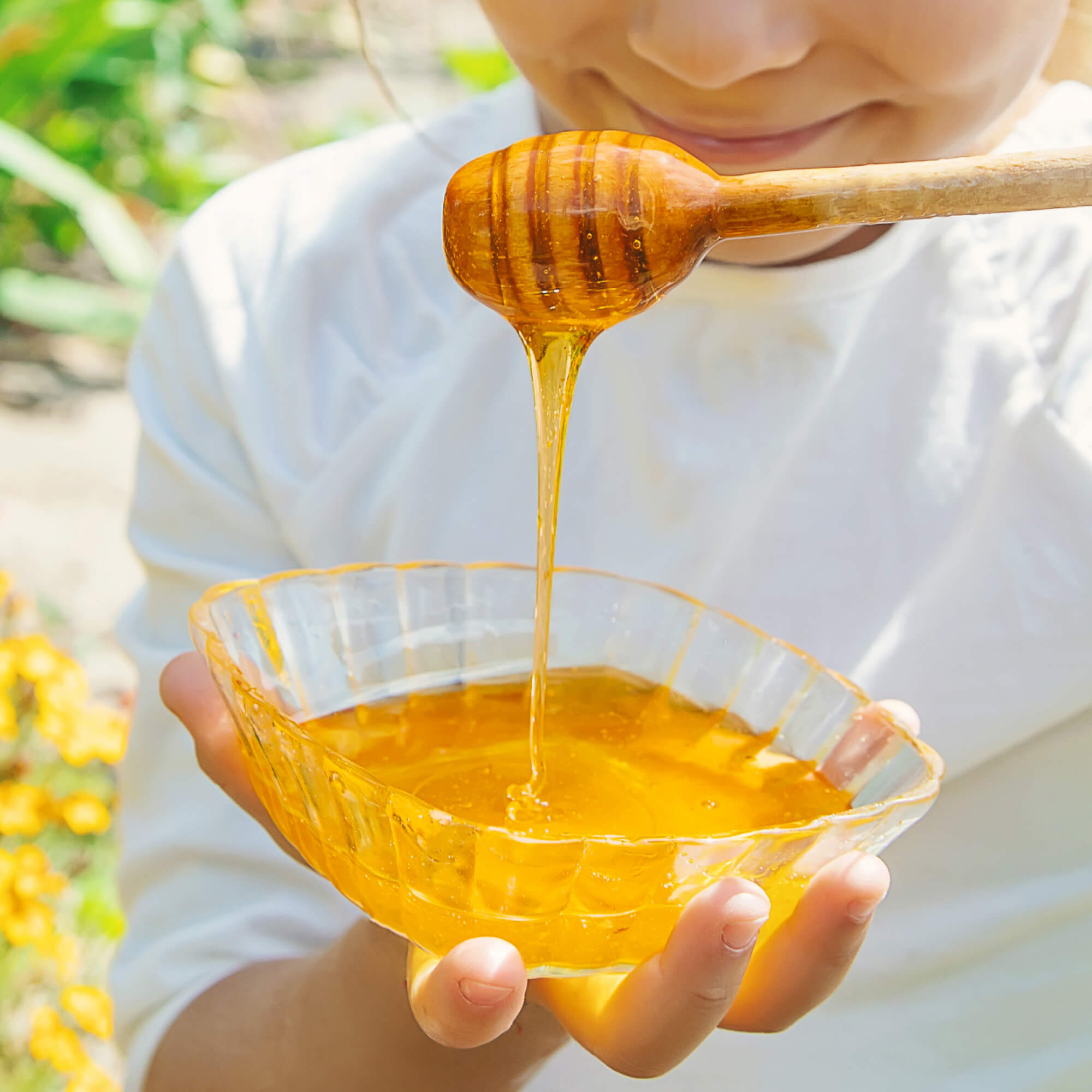 Person holding a bowl of Matauwhi kanuka honey with a wooden honey dipper outdoors.