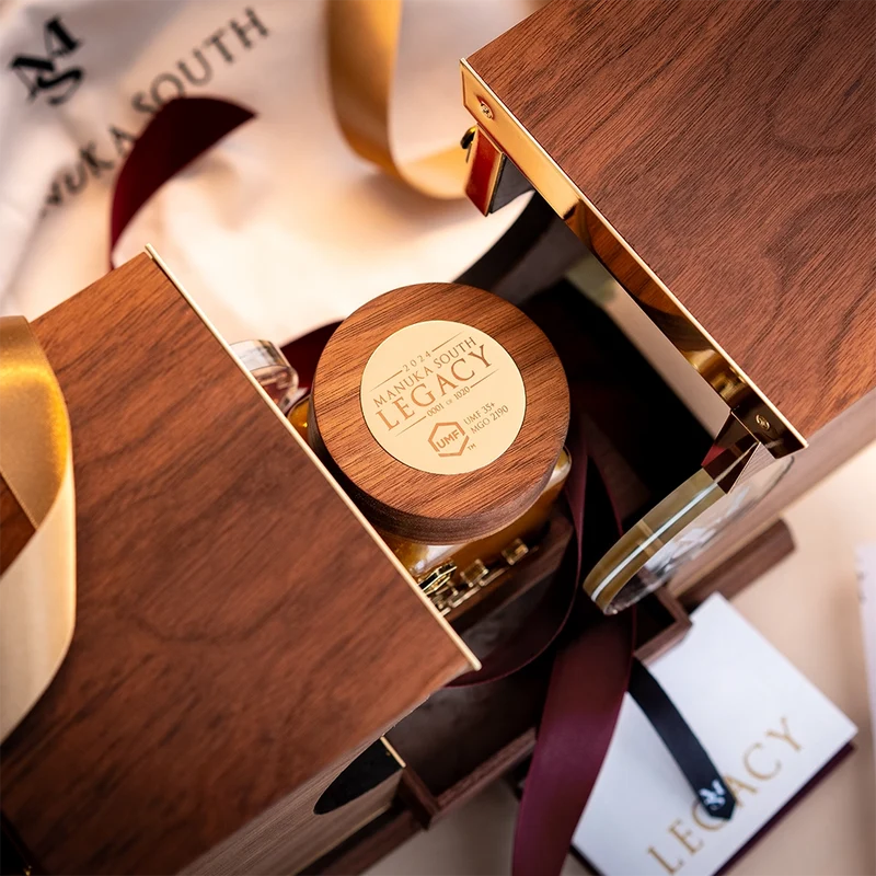 A luxury gift set from Maranda South Legacy, featuring a wooden jar with a branded lid nestled inside an open wooden presentation box with gold trim and a cream ribbon. Manuka South Manuka Honey UMF35+.