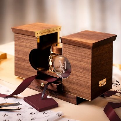 A luxury Manuka Honey jar with a clear glass insert and gold details, presented in a custom wooden display box with a dark burgundy ribbon, on a beige surface with branded papers.