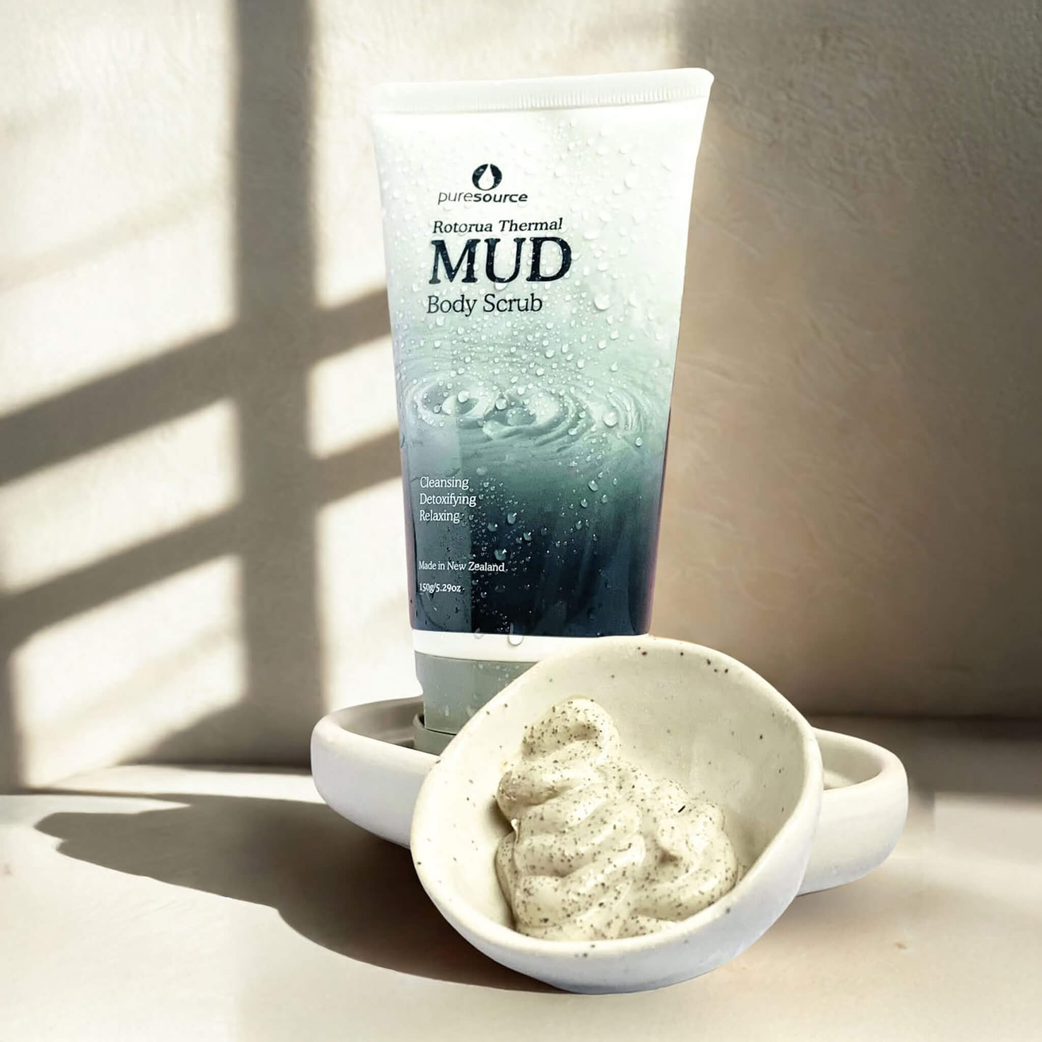Tube of Mud Body Scrub with a small dish of scrub on a neutral background
