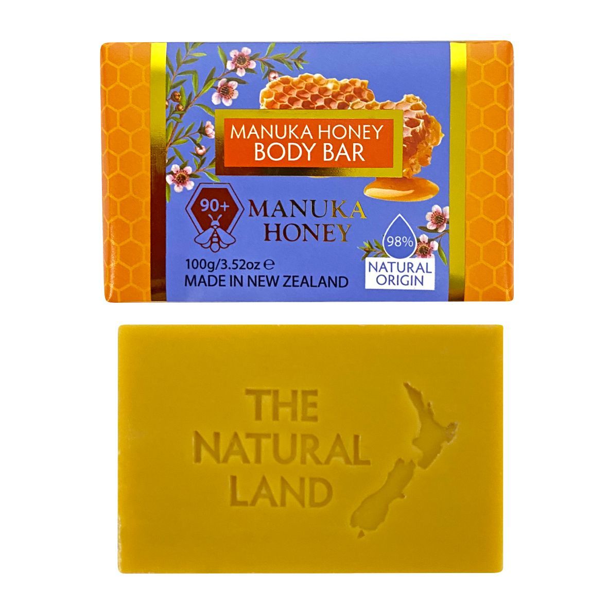 A manuka honey body bar soap shown in two views: the wrapped bar at the top with a blue and orange label, and the unwrapped yellow soap bar at the bottom embossed with 'THE NATURAL LAND' and a New Zealand map outline.