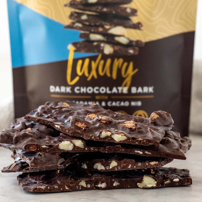 Dark chocolate bark with macadamia nuts in front of a 'Luxury Dark Chocolate Bark' packaging.