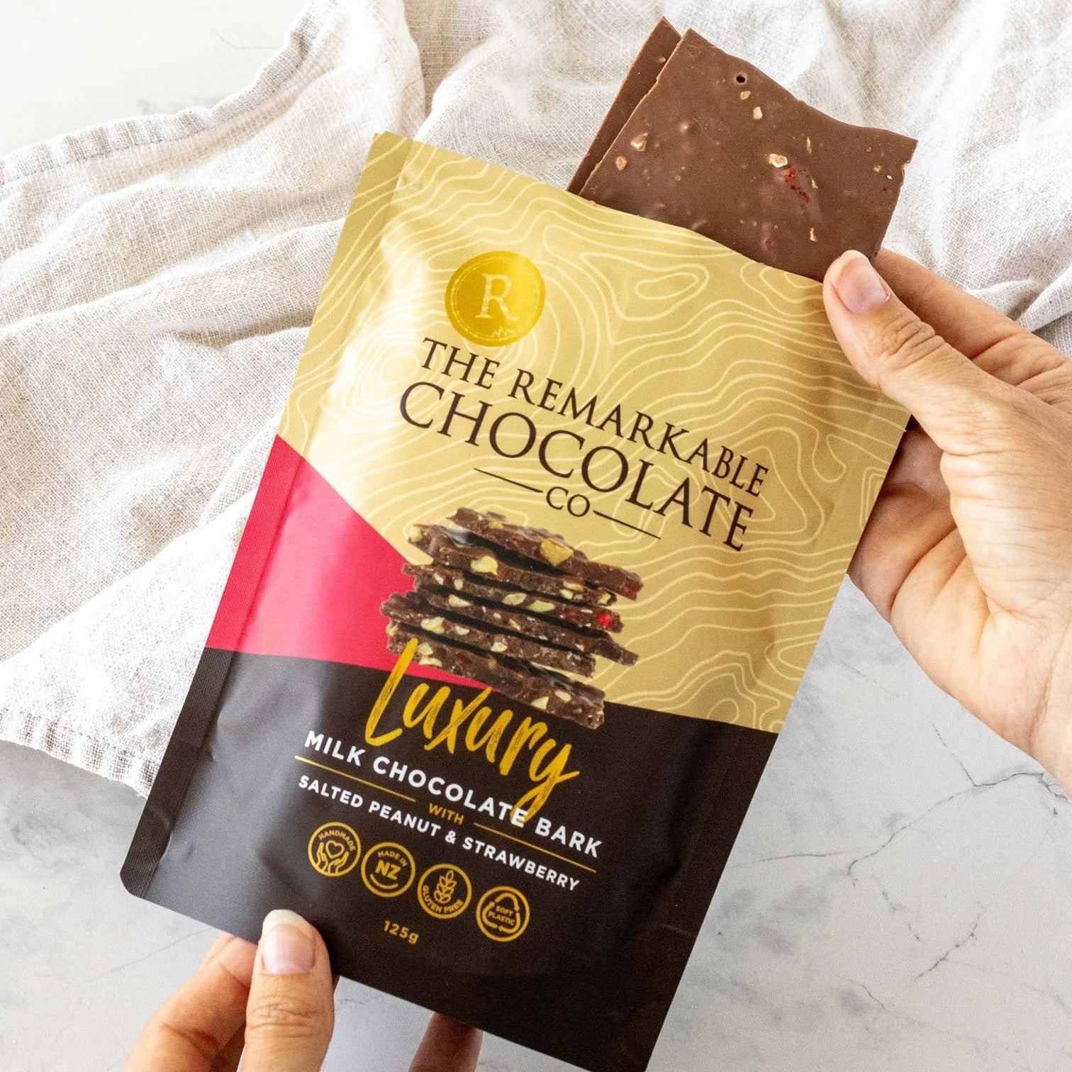 Hand holding a package of The Remarkable Chocolate Co. Luxury Milk Chocolate Bark Salted penut and  Strawberry