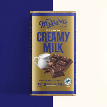 A single Whittaker's Creamy Milk chocolate bar in its packaging, shown against a split blue and off-white background.