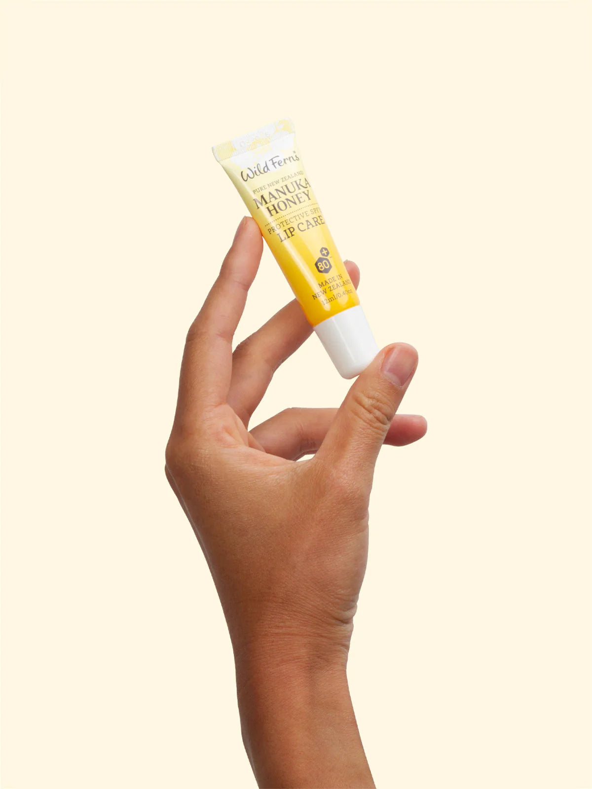 Hand holding a tube of Wild Ferns Manuka Honey lip balm against a light background