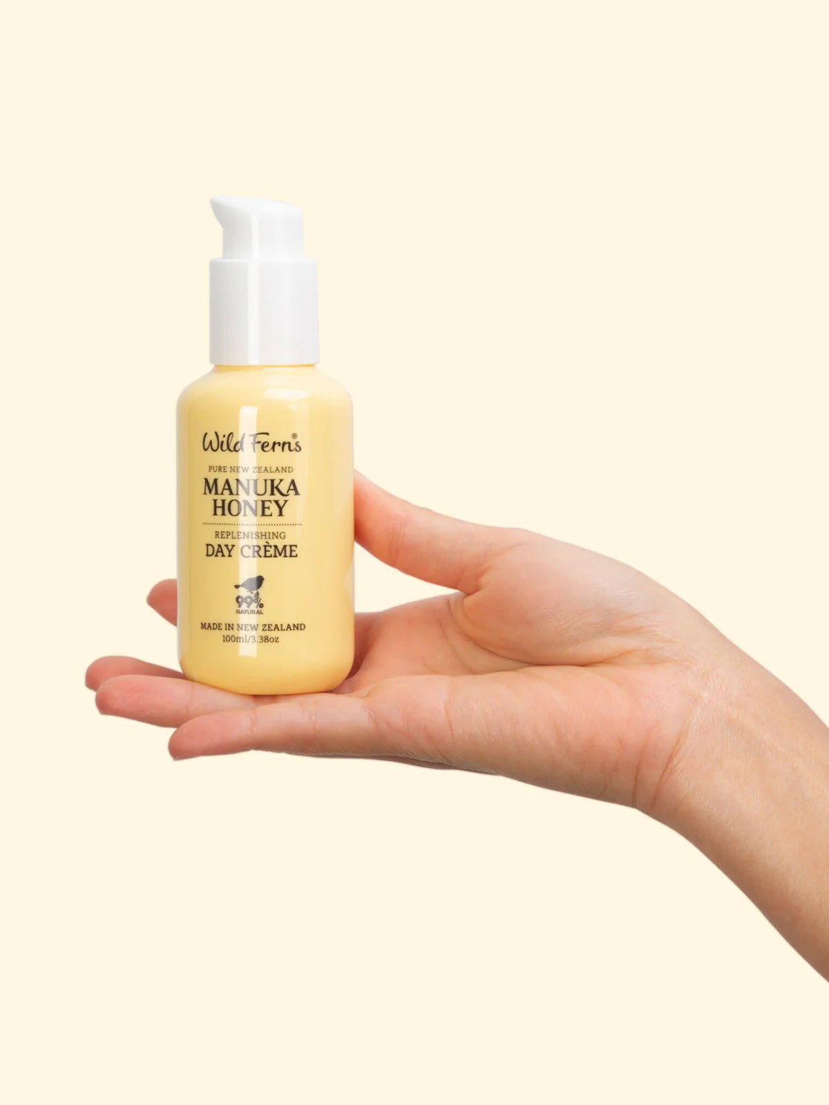 Hand holding a bottle of Wild Ferns Manuka Honey Day Creme against a beige background