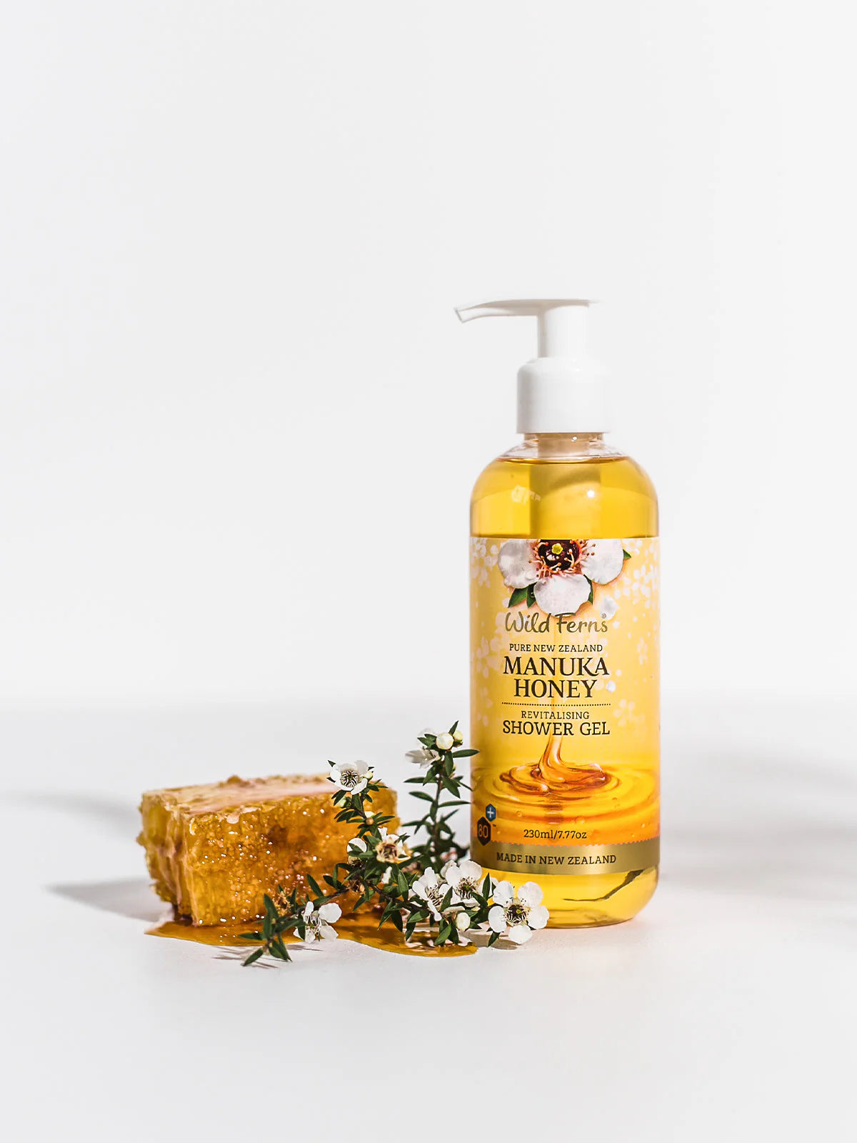 Bottle of Wild Ferns Mānuka Honey Shower Gel with honeycomb and flowers on a white background