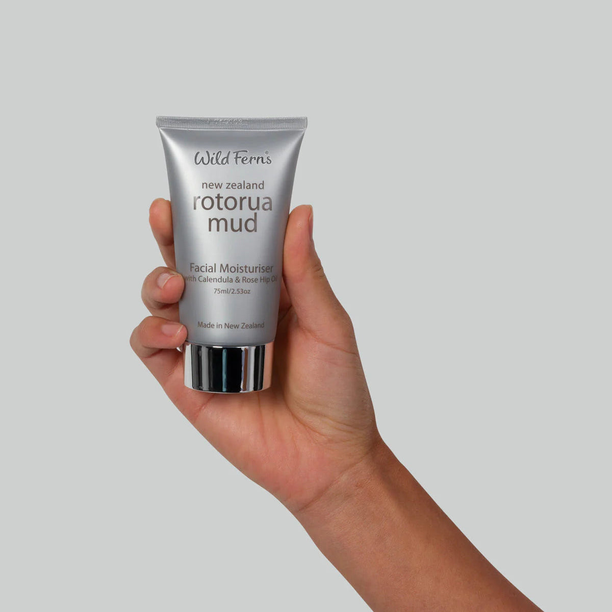 Hand holding a tube of Wild Ferns Rotorua Mud Facial Moisturiser against a plain background