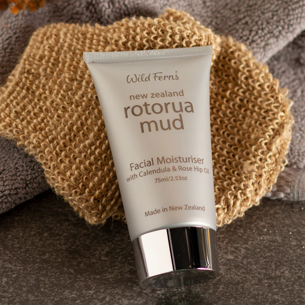 Tube of Wild Ferns Rotorua Mud Facial Moisturizer on a textured surface with a sponge and towel.