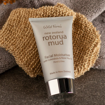 Tube of Wild Ferns Rotorua Mud Facial Moisturizer on a textured surface with a sponge and towel.