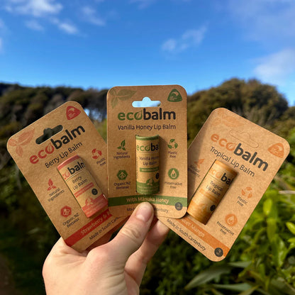 Hand holding three packages of ecoBalm lip balm against a natural background