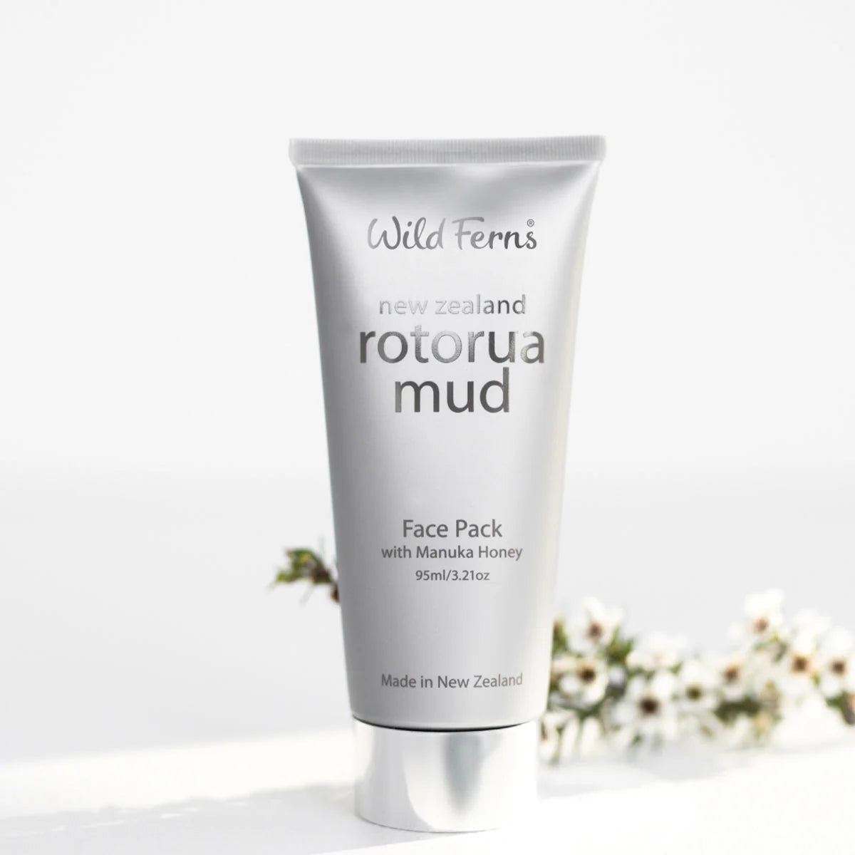 Tube of Wild Ferns Rotorua Mud Face Pack on a white background with blurred flowers.