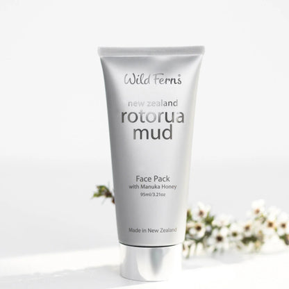 Tube of Wild Ferns Rotorua Mud Face Pack on a white background with blurred flowers.