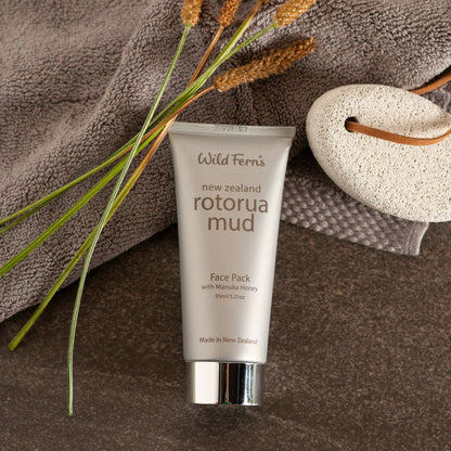 Tube of Wild Ferns Rotorua Mud Face Pack on a brown towel with plants and a loofah.